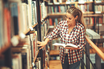 Wall Mural - Young female student read and learns by the book shelf at the library.