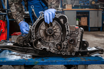 A close-up of a young man repairman in a working uniform of cars is repairing an automatic gearbox of a used car in an auto repair shop. The concept of car repair and car repair shop