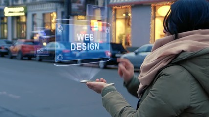 Unrecognizable woman standing on the street interacts HUD hologram with text Web Design. Girl in warm clothes with a scarf uses technology of the future mobile screen on background of night city