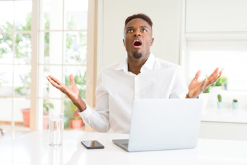 Poster - African american business man working using laptop crazy and mad shouting and yelling with aggressive expression and arms raised. Frustration concept.