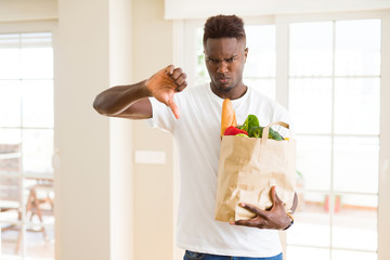 Poster - African american man holding paper bag full of fresh groceries with angry face, negative sign showing dislike with thumbs down, rejection concept