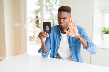 Sticker - African american man holding passport of Canada with open hand doing stop sign with serious and confident expression, defense gesture