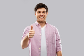 gesture and people concept - happy young man showing thumbs up over grey background