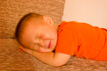 Boy in orange t-shirt sleeping on the couch at home. Close up