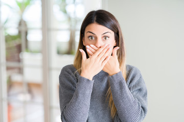 Wall Mural - Young beautiful woman wearing winter sweater at home shocked covering mouth with hands for mistake. Secret concept.