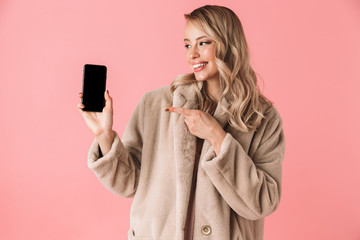 Poster - Beautiful happy young pretty woman posing isolated over pink wall background showing display of mobile phone.