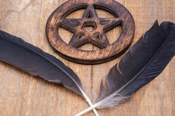 Two Black Raven feathers and Wooden encircled Pentagram symbol on wood background. Five elements: Earth, Water, Air, Fire, Spirit. 