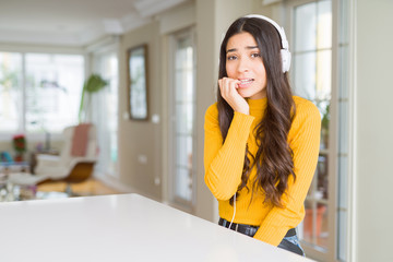 Poster - Young woman wearing headphones listening to music looking stressed and nervous with hands on mouth biting nails. Anxiety problem.