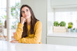 © Krakenimages.com - Beautiful young woman wearing yellow sweater with hand on chin thinking about question, pensive expression. Smiling with thoughtful face. Doubt concept.