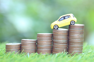 Miniature yellow car model on growing stack of coins money on nature green background, Saving money for car, Finance and car loan, Investment and business concept