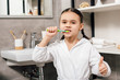 © LIGHTFIELD STUDIOS - child in white bathrobe brushing teeth and showing thumb up in bathroom