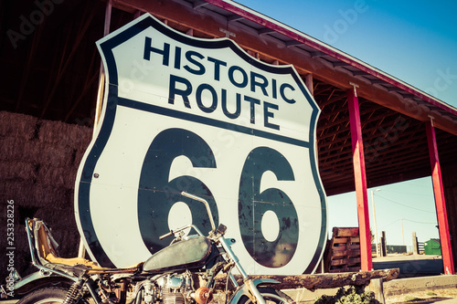 A large Route 66 road sign with a weathered motorcycle in the foreground Canvas Print