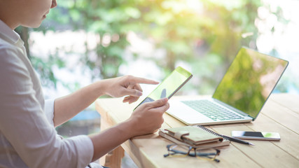 Young Asian business man using digital tablet working with laptop computer and smartphone in coworking space. Urban lifestyle with modern electronic devices. Internet of things and online app concepts