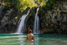 Young Plump Red-haired White Woman With A Bare Back Is Standing In The Turquoise Water Of A Beautiful Waterfall Among The Rocks In The Jungle