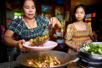 Wall Mural - thai mother and daughter plating freshly cooked red curry in rustic traditional kitchen