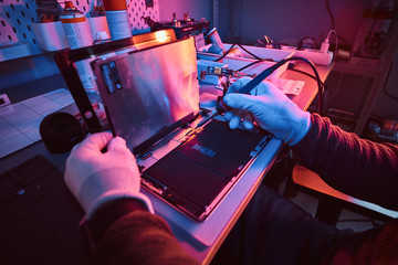 Wall Mural - The technician repairs a broken tablet computer in a modern repair shop. Illumination with red and blue lights