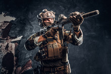 Elite Unit, Special Forces Soldier In Camouflage Uniform Holding An Assault Rifle With A Laser Sight And Aims At The Target. Studio Photo Against A Dark Textured Wall