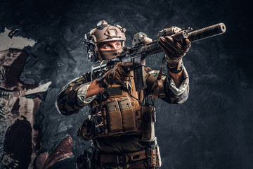 Elite unit, special forces soldier in camouflage uniform holding an assault rifle with a laser sight and aims at the target. Studio photo against a dark textured wall