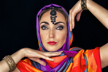 East woman in burqa with jewels on a black background. A woman in a bright scarf is dancing.