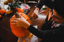 Close-up Of Boy Carving Pumpkin For Jack O' Lantern While Sitting At Home
