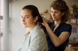 © Erickson Stock - Portrait of a teenage girl getting her hair fixed by her mother inside their home.