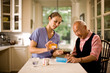 © Erickson Stock - Nurse and senior man discussing medication in a kitchen.