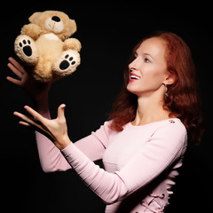 Red-haired girl model posing with a teddy bear. On a black backg