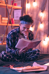 Playful boy finding a humor in thick book about nature and health, and even forgetting about the pizza.