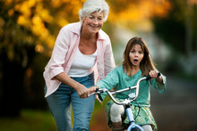 Little Girl Learning To Ride Her Bicycle With The Help Of Her Grandmother.