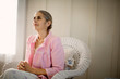 © Erickson Stock - Contemplative senior woman sitting in an armchair with her hands clasped.