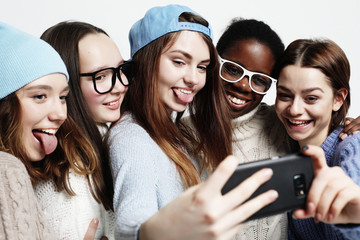 five multiethnic girls laughing and taking selfie isolated over white background