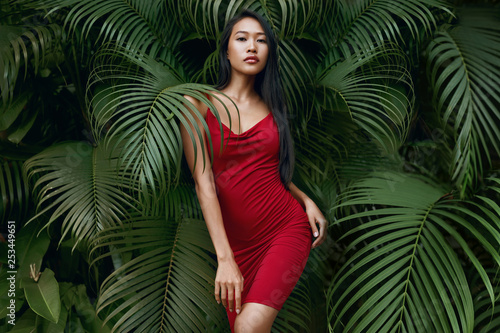 Fashion. Woman model in red dress with green palm leaves Tableau sur Toile
