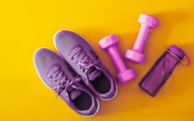 Canvas Print - Top view of purple and violet sport shoes, dumbbells and bottle of water on yellow background. Fitness and Healthy lifestyle background concept.