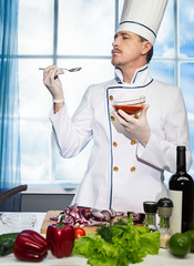 Wall Mural - Cook in white uniform stands tests the sauce from the spoon in the kitchen