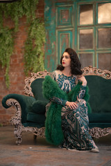 elegant caucasian girl in a luxurious long sequins lace dress with a green fluffy boa in her hands posing in the retro room with vintage luxury furniture