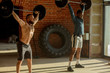© alfa27 - Couple of shirtless interracial male athletes pumping muscles with heavy weight barbell at indoor crossfit studio. Men doing weight lifting.
