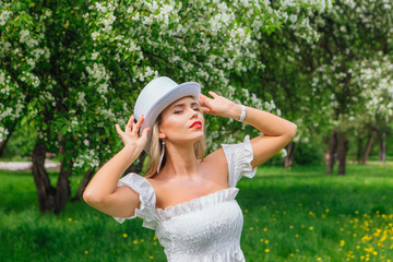 Sexy modern bride in white cylinder hat enjoing bloomin apple tree flowers.