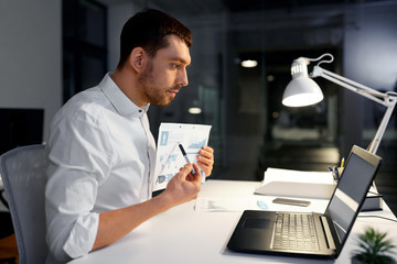 Canvas Print - business, technology and people concept - businessman with charts having video chat on laptop computer at night office