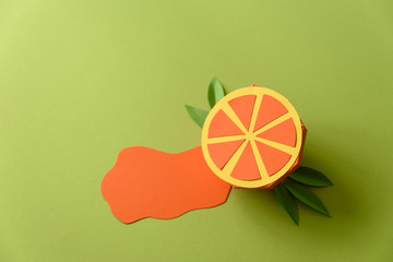 Spilled juice and paper orange fruit on green background. Copy space. Creative or art food concept