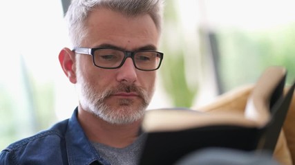 Wall Mural - Mature man wearing glasses reading book at home