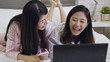© PRPicturesProduction - Two young asian girls sitting lying at laptop look at monitor chatting with friends over video chat in a light interior in loft style. women in pajamas watching humour talk show on computer laughing