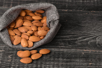 Almonds in gray bag on textured  dark wooden background, top view. Copy space.