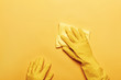 A hands in a rubber protective glove with a white sponge on a yellow background. Cleaning concept.