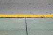 A cement sidewalk with yellow painted curb and part of street on a sunny morning.