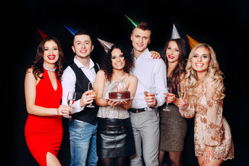 Wall Mural - Pretty girl with birthday cake and her friends looking at burning candles at party