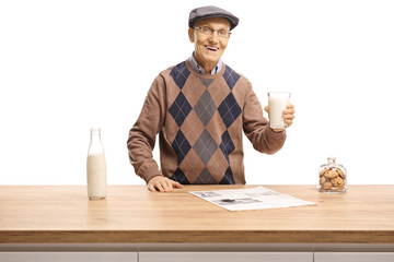 Wall Mural - Elderly man holding a glass of milk and standing behind a wooden counter