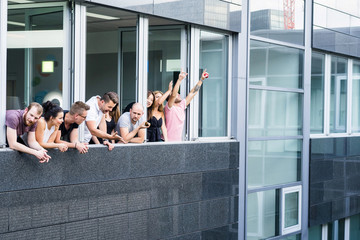 group of young people standing in an office with a large window