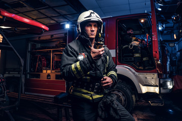 Wall Mural - The fire brigade arrived at the night-time. Fireman in a protective uniform standing next to a fire truck and talking on the radio