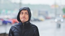 Portrait Of A Young Man In A Jacket With A Hood In The Rain On Blurred Background City Street, Close-up