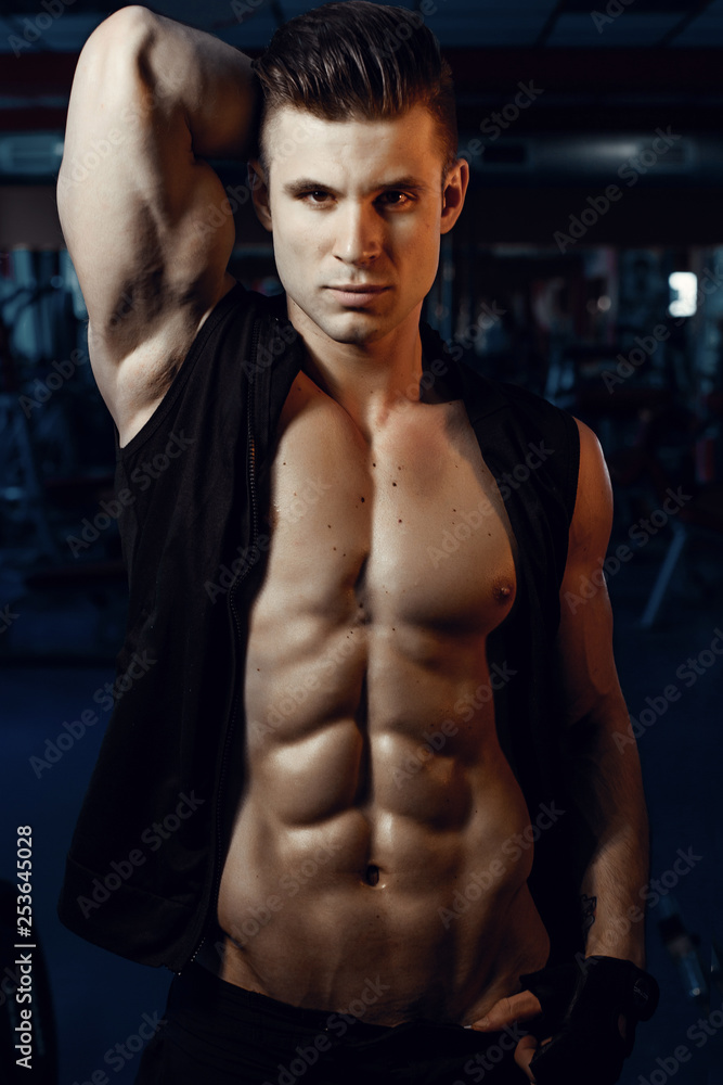Muscular model young man exercising in gym. Portrait of sporty strong